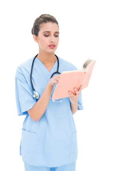 Bezorgd verpleegster in blauw scrubs lezen van een boek — Stockfoto