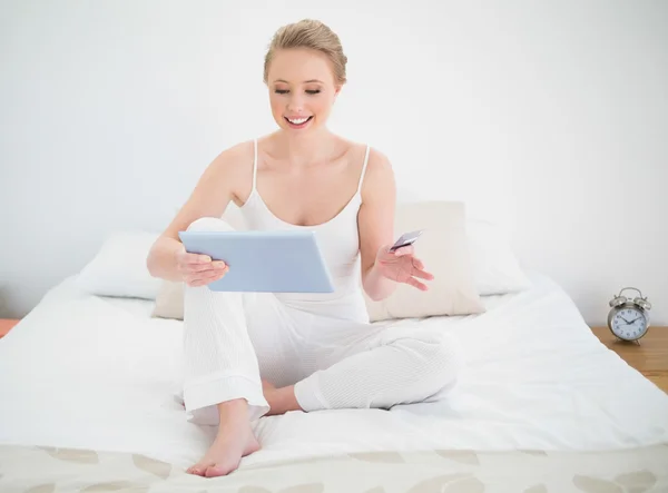Natural rubia sonriente mirando la tableta mientras está sentado en la cama — Foto de Stock