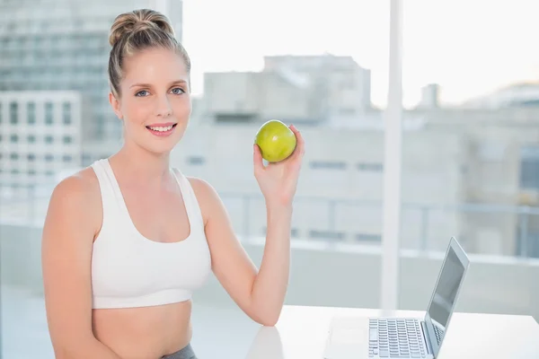 Sonriente rubia deportiva sosteniendo manzana verde — Foto de Stock