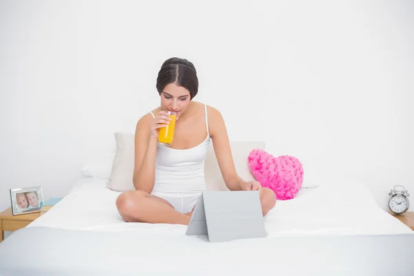 Vreedzame jonge model in witte pyjama's drinken sinaasappelsap — Stockfoto