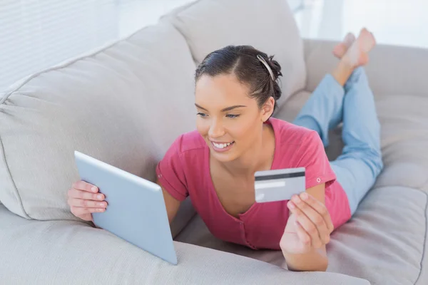 Attractive woman making an online payment with her credit card while lying on a sofa — Stock Photo, Image