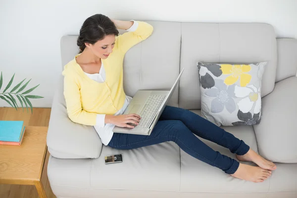 Entspannte lässige Brünette in gelber Strickjacke tippt auf Laptop — Stockfoto