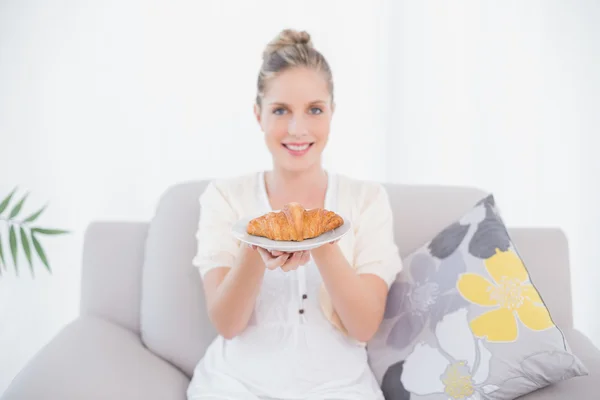 Modelo fresco alegre segurando croissant sentado no sofá — Fotografia de Stock