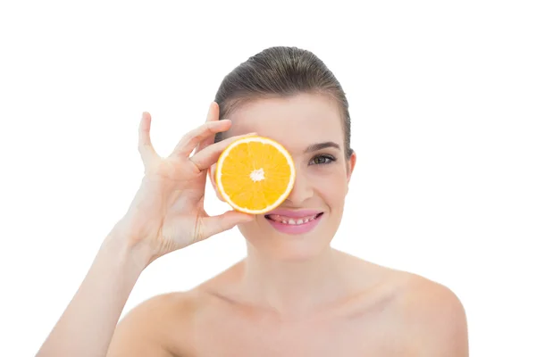 Cheerful model hiding her eye with an orange half — Stock Photo, Image