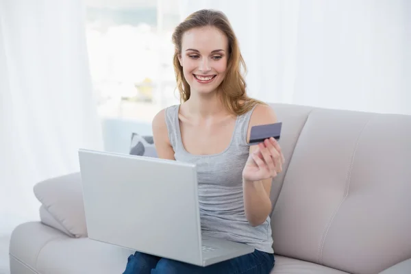 Jovem alegre sentada no sofá usando laptop para compras on-line — Fotografia de Stock