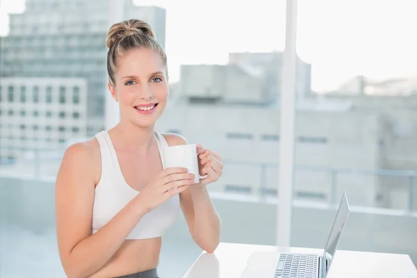 Smiling athletic blonde holding coffee — Stock Photo, Image