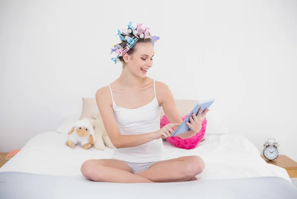 Delighted woman in hair curlers using a tablet pc — Stock Photo, Image