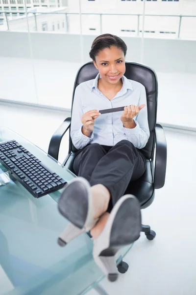 Fröhliche junge Geschäftsfrau feilt an ihren Nägeln, während sie am Schreibtisch sitzt — Stockfoto