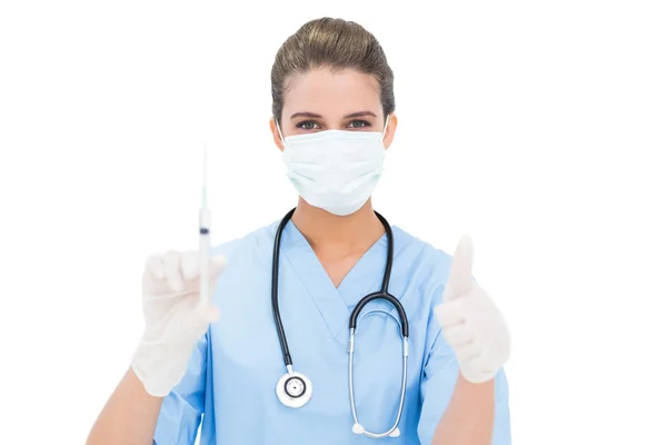 Beautiful nurse in blue scrubs holding a syringe and giving a thumb up — Stock Photo, Image