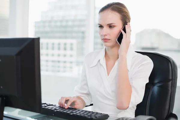 Serious businesswoman sitting at desk talking on smartphone looking at screen — Stock Photo, Image