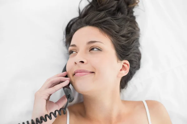 Happy casual brunette in white pajamas calling with a telephone — Stock Photo, Image