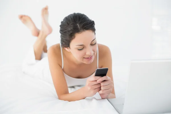 Calma morena casual em pijama branco usando seu telefone celular — Fotografia de Stock
