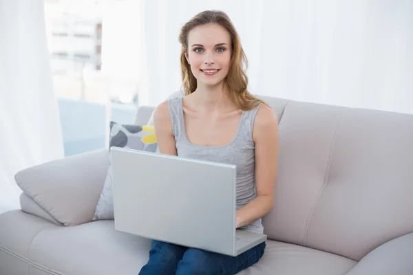 Happy young woman sitting on couch using laptop — Stock Photo, Image