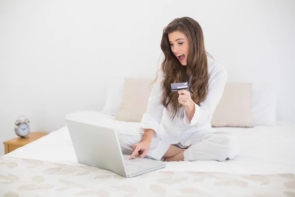 Έκπληκτος γυναίκα στο λευκό πιτζάμες online αγορές με το laptop — Φωτογραφία Αρχείου