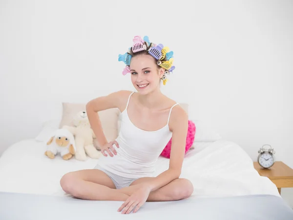 Cheerful woman in hair curlers sitting on her bed — Stock Photo, Image