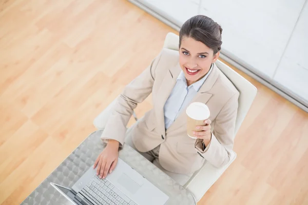 Geschäftsfrau hält eine Tasse Kaffee während sie einen Laptop benutzt — Stockfoto