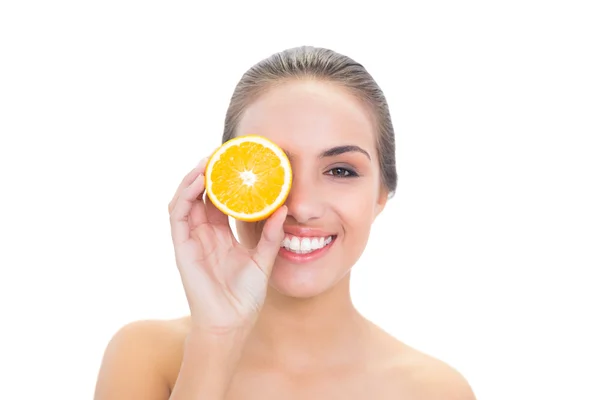 Cheerful woman holding an orange half in front of her eye — Stock Photo, Image