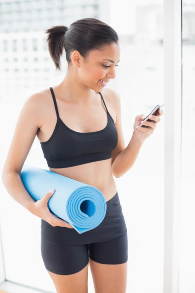 Modelo estampado em sportswear carregando um tapete de exercício e usando um telefone celular — Fotografia de Stock