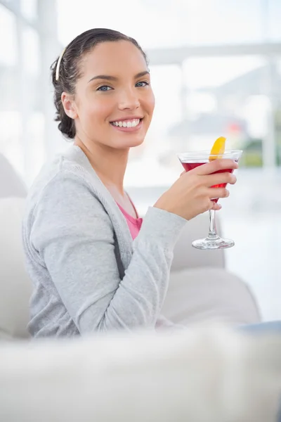Happy woman sitting on sofa and holding cocktail — Stock Photo, Image