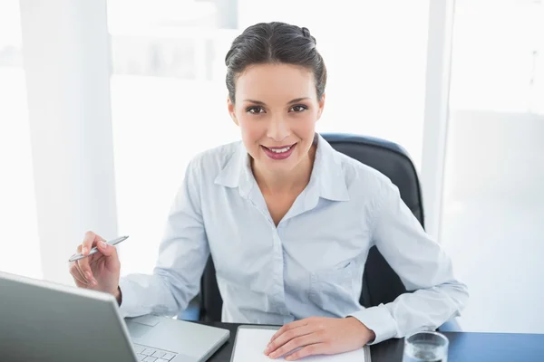 Heureuse femme d'affaires brune élégante prenant des notes et regardant la caméra — Photo