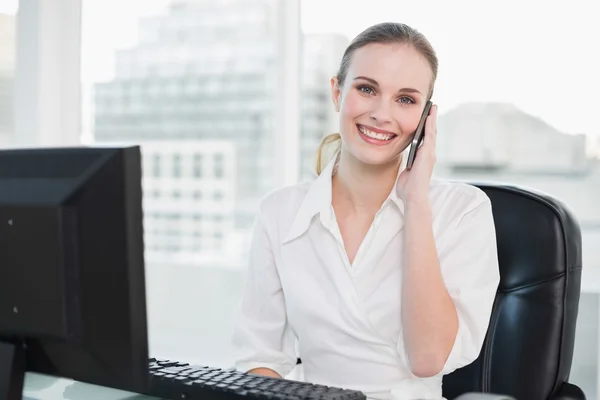 Zufriedene Geschäftsfrau sitzt am Schreibtisch und telefoniert mit dem Smartphone — Stockfoto