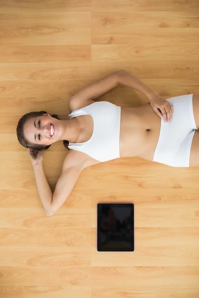 Vrolijke sportieve brunette liggen naast een tablet — Stockfoto