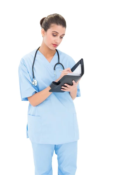 Συγκεντρωμένη νοσοκόμα σε μπλε τρίβει πλήρωση μια ατζέντα — Φωτογραφία Αρχείου