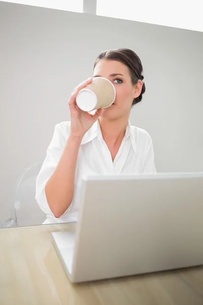 Businesswoman drinking coffee while using laptop — Stock Photo, Image