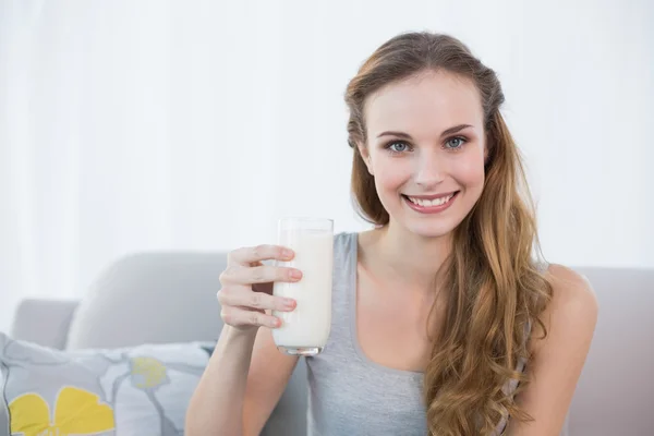 Jovem feliz sentada no sofá segurando um copo de leite — Fotografia de Stock