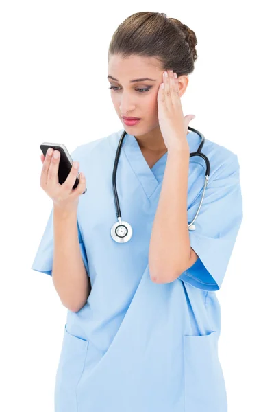Infirmière perplexe en blouse bleue utilisant un téléphone portable — Photo