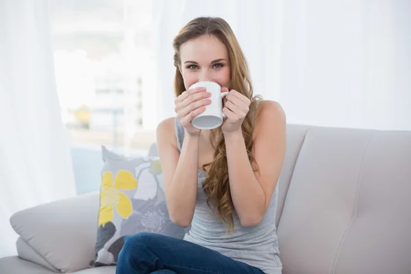 Jovem feliz sentada no sofá bebendo de uma caneca — Fotografia de Stock