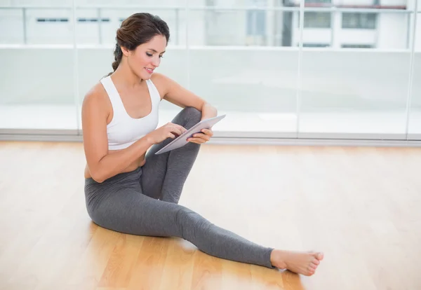 Sportivo felice bruna utilizzando tablet seduto sul pavimento — Foto Stock