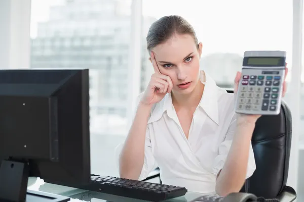 Frowning donna d'affari mostrando calcolatrice seduta alla scrivania — Foto Stock