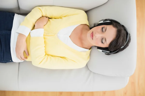Peaceful casual brunette in yellow cardigan listening to music with headphones — Stock Photo, Image