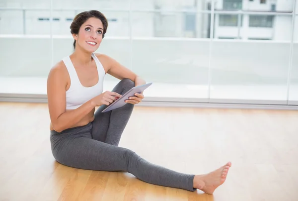 Sportieve doordachte brunette met behulp van Tablet PC zittend op de vloer — Stockfoto