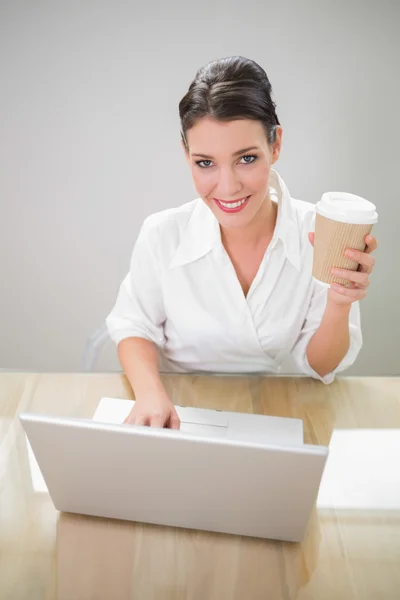 Affärskvinna hålla kaffe medan du använder laptop — Stockfoto