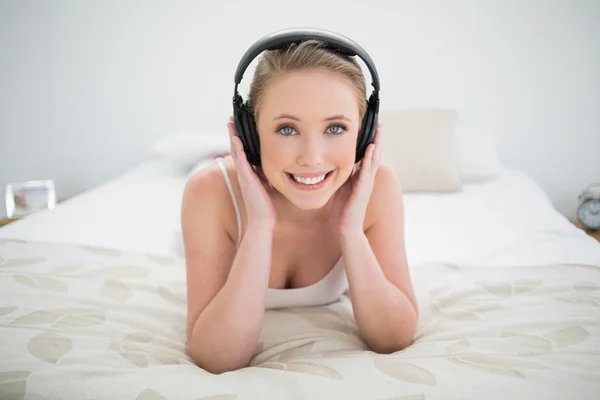 Φυσικό ευτυχής ξανθιά ξαπλωμένος στο κρεβάτι και να ακούτε μουσική — Φωτογραφία Αρχείου