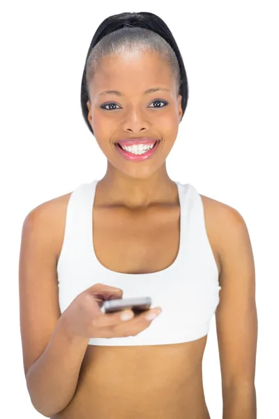 Lachende vrouw in sportkleding telefoon te houden terwijl de camera kijken — Stockfoto