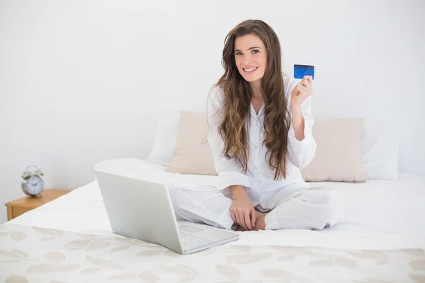Mujer contenta en pijama blanco de compras en línea con su computadora portátil —  Fotos de Stock