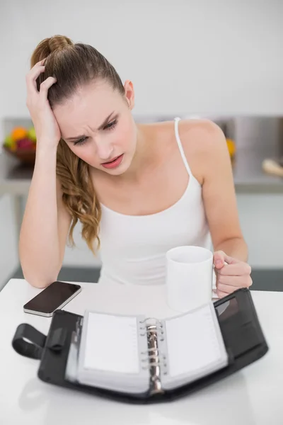 Jovem estressada segurando uma caneca olhando para o diário aberto — Fotografia de Stock