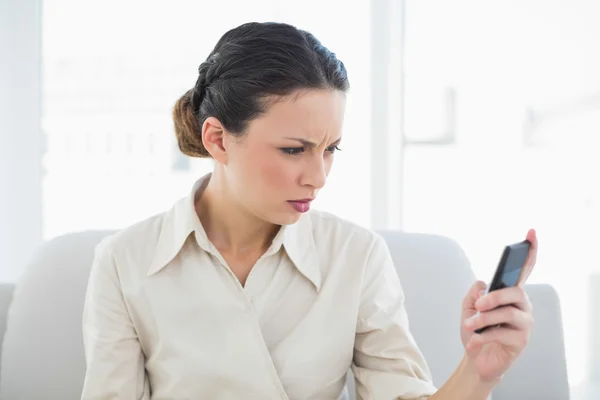 Rynkar pannan snygg brunett affärskvinna tittar på sin mobiltelefon — Stockfoto