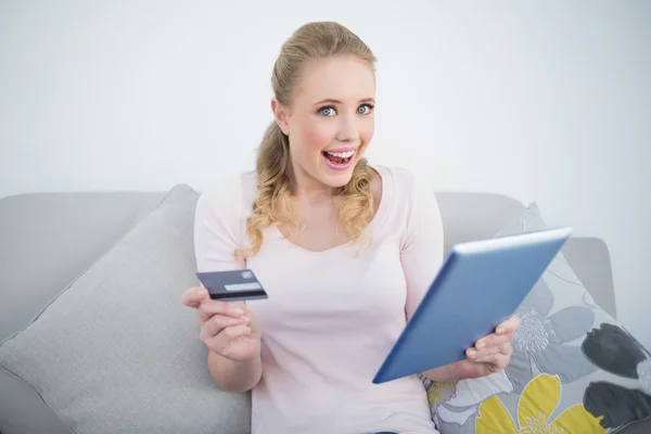 Casual opgewonden blonde bedrijf tablet en credit card — Stockfoto