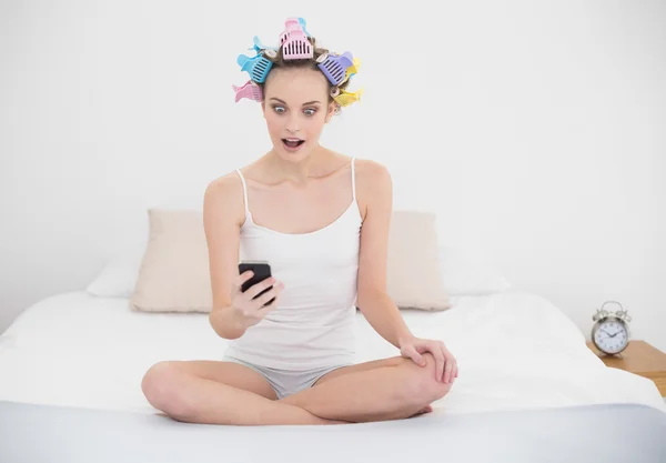 Diví se žena v natáčky na vlasy při pohledu na její mobilní telefon — Stock fotografie