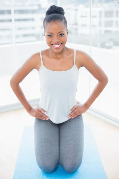 Femme souriante assise sur un tapis d'exercice avec les mains sur la hanche — Photo