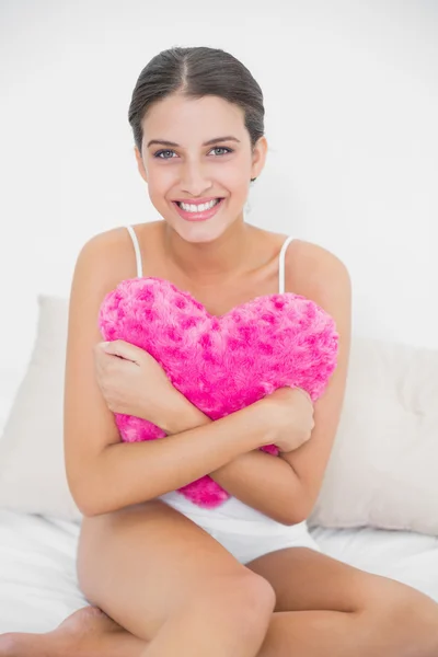 Modello in pigiama bianco che abbraccia un cuscino a forma di cuore — Foto Stock