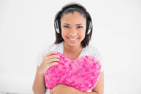 Joyful young model cuddling a pillow and listening to music — Stock Photo, Image