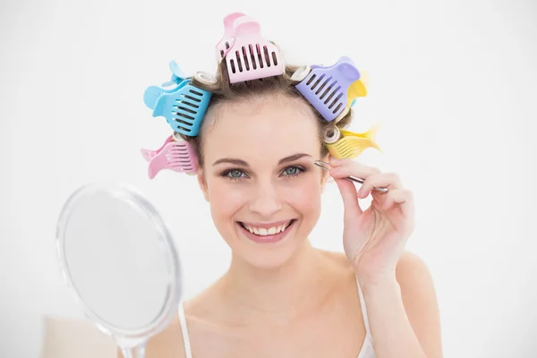 Charming woman in hair curlers plucking her eyebrows — Stock Photo, Image