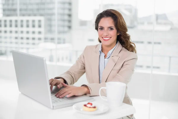 Cheerful businesswoman using laptop at her desk and having coffee — Stock Photo, Image