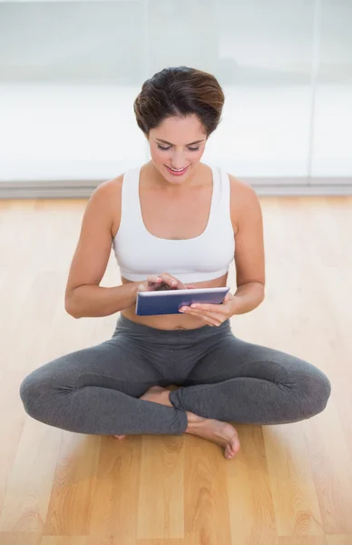 Sportig glad brunett sitter i lotus pose och använder tablet — Stockfoto