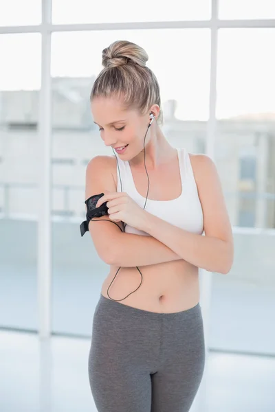 Smiling sporty blonde changing music on her mp3 player — Stock Photo, Image